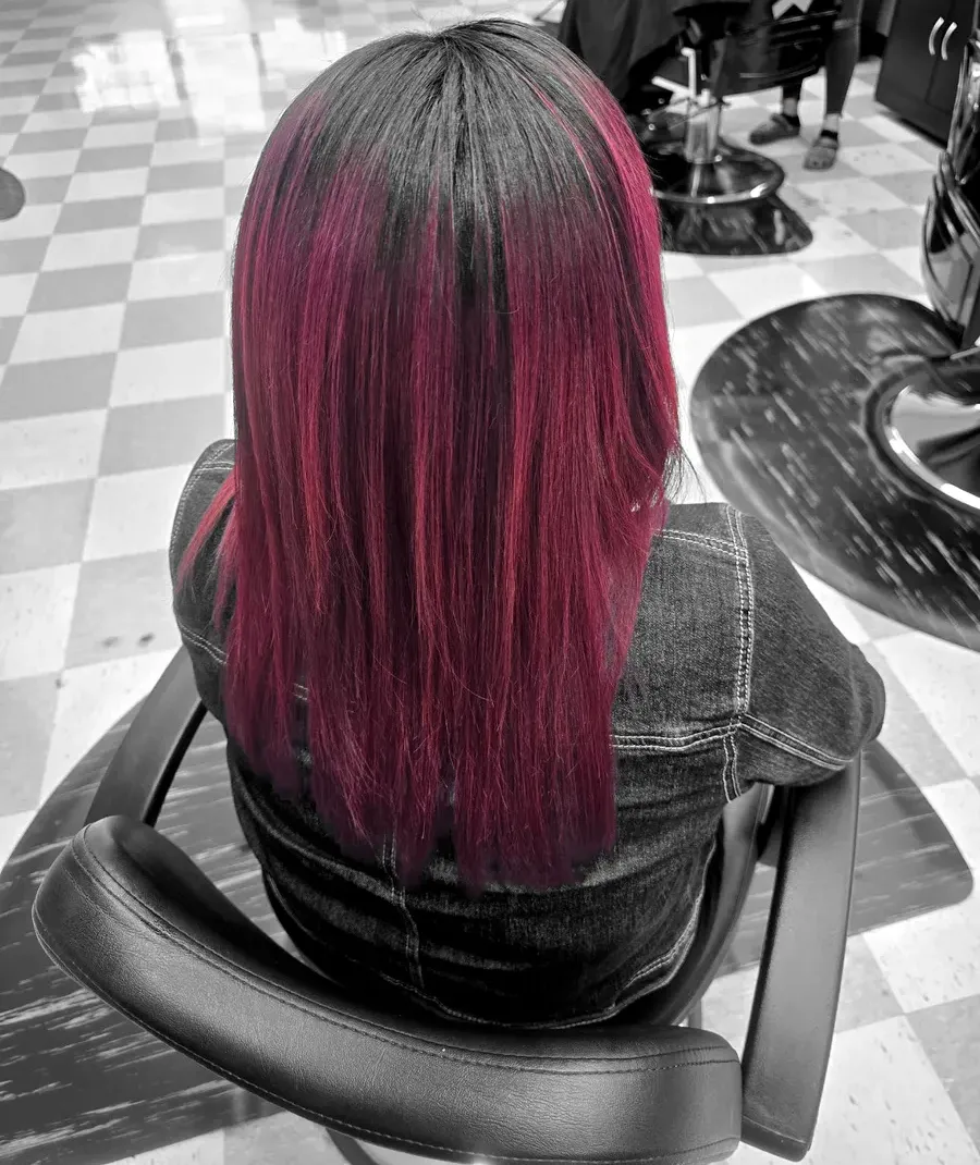 Long hair finished in a deep magenta-wine colour, seen from behind in a Bellas styling chair on the checkered floor